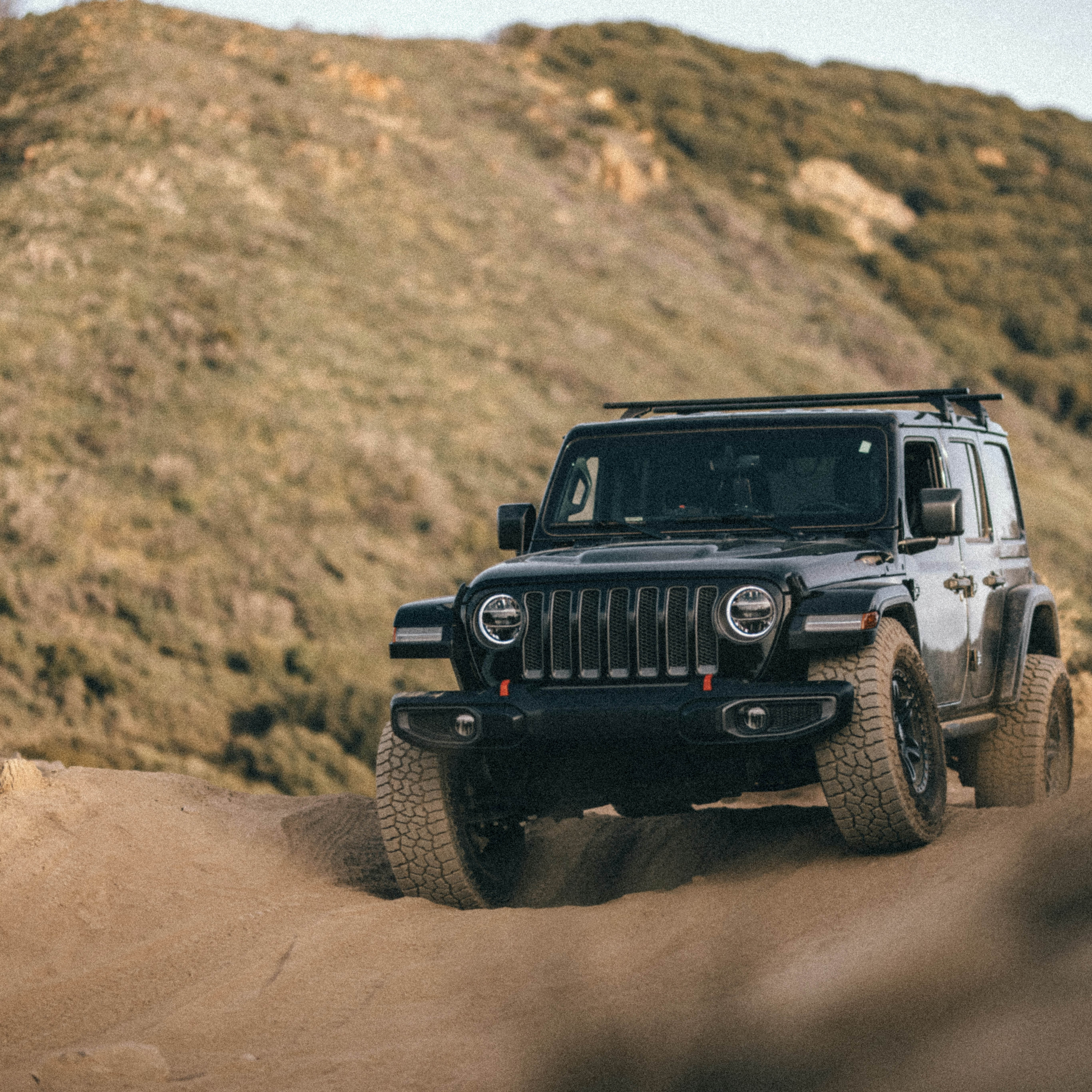 Black off-road SUV driving on a dirt trail with hills in the background.