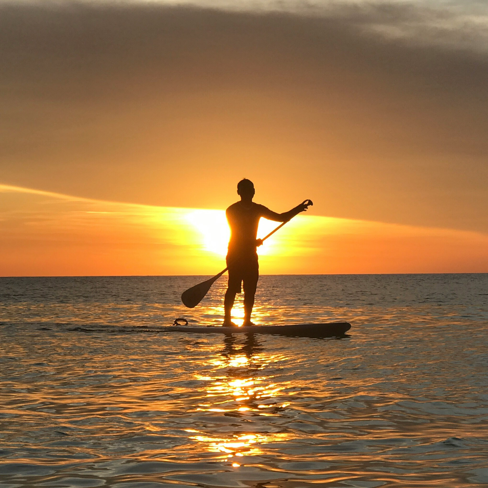 Silhouette of a person paddleboarding on calm water during a golden sunset.