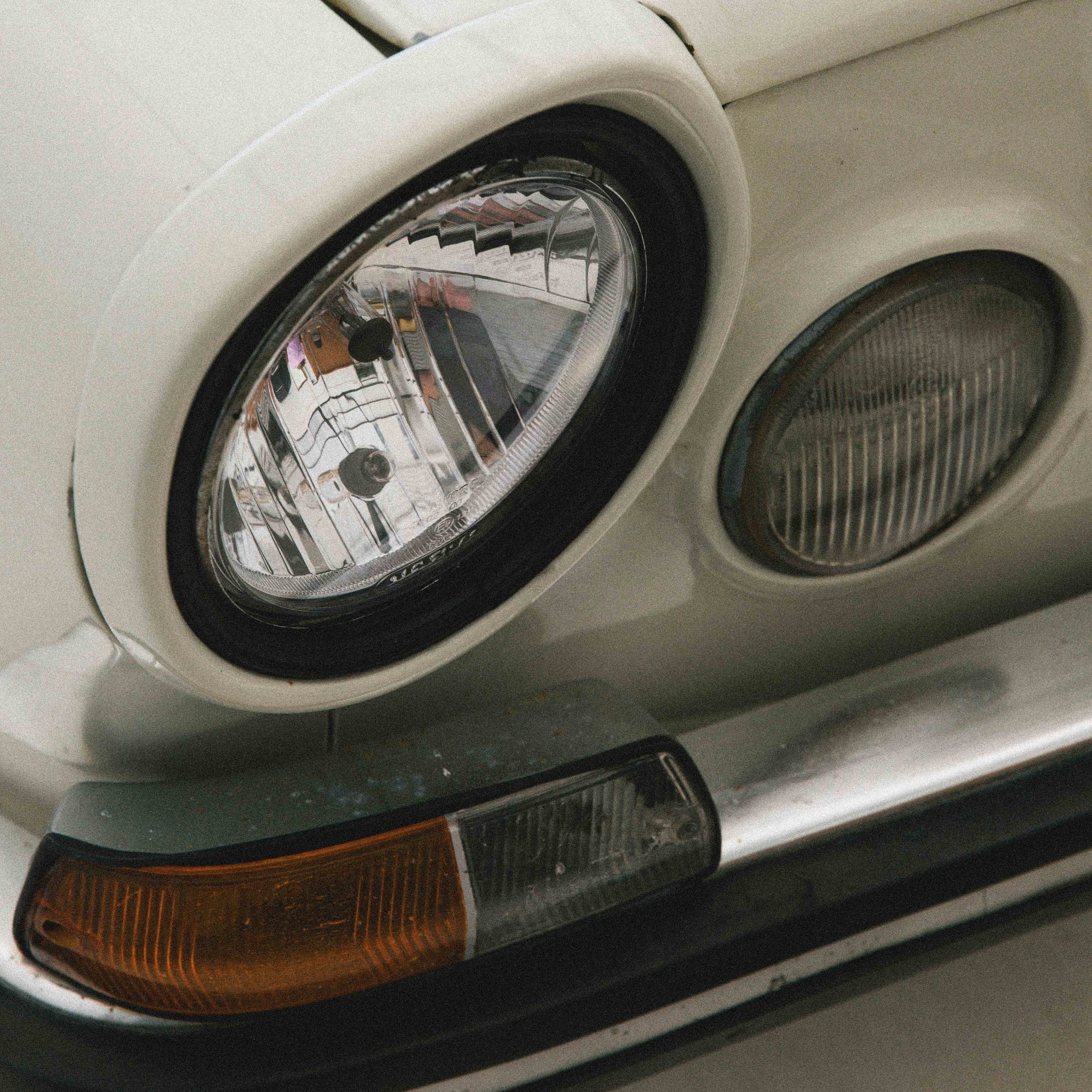 Close-up of vintage car headlights and front indicator light with chrome bumper.
