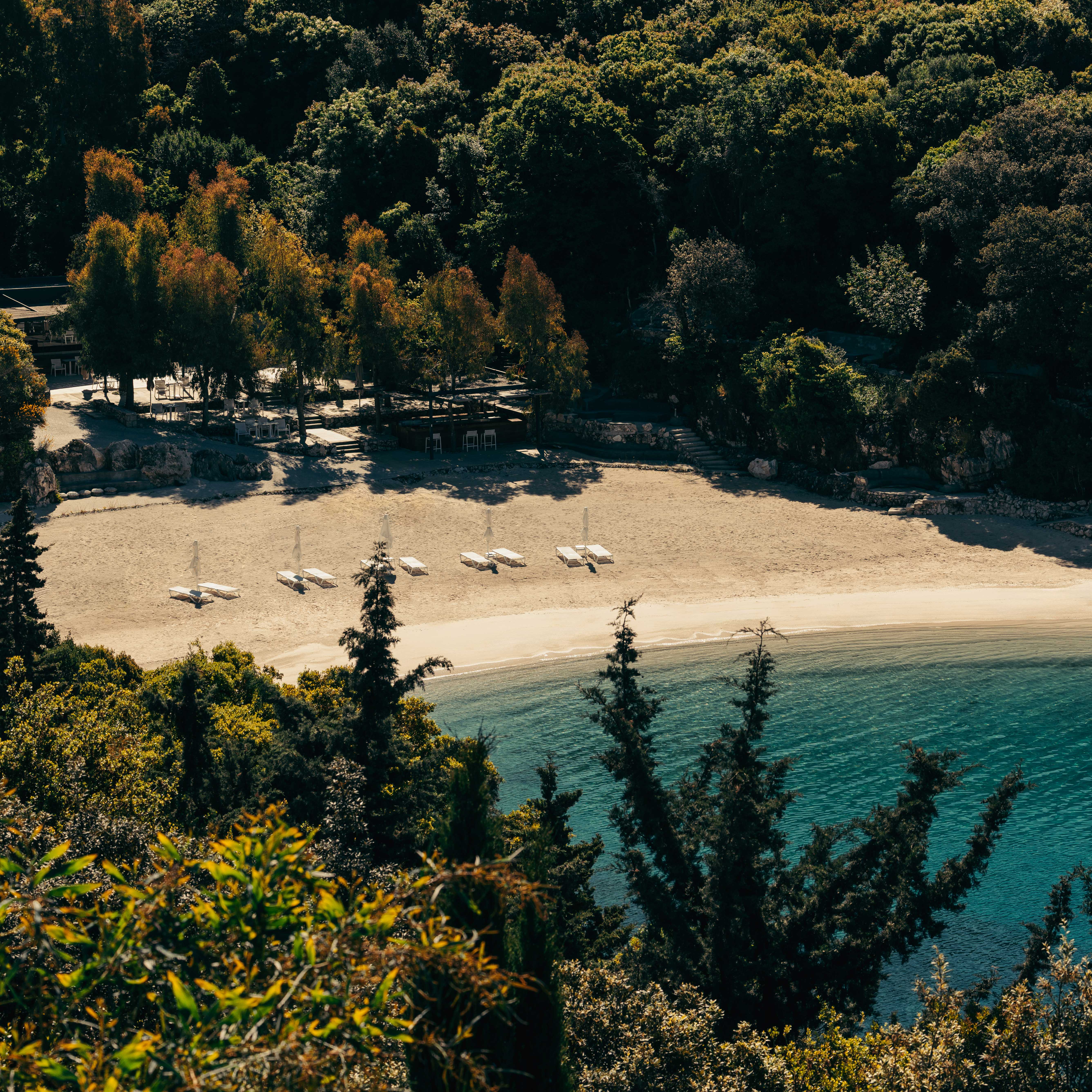 Secluded beach with sun loungers and umbrellas along a turquoise shoreline bordered by dense green forest.