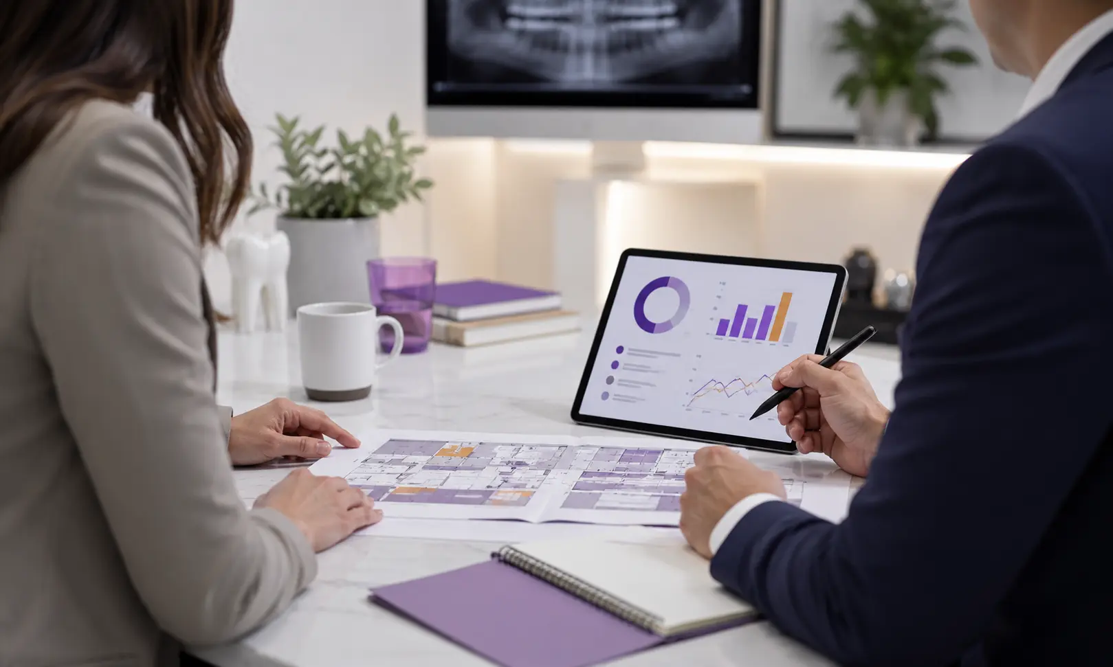Two people reviewing building plans and analytics charts on a tablet at a white desk.