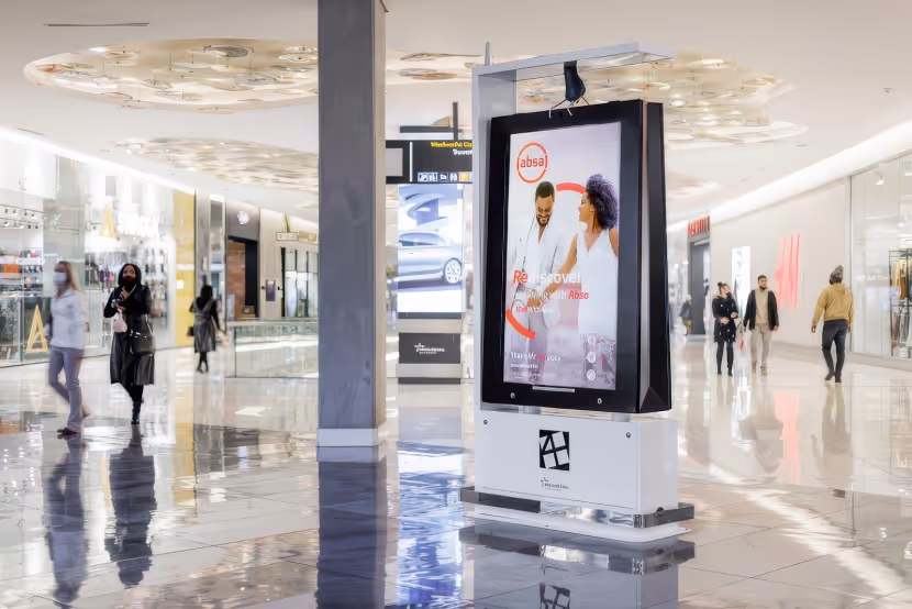 Indoor mall scene with digital advertising board and people walking on shiny tiled floor.