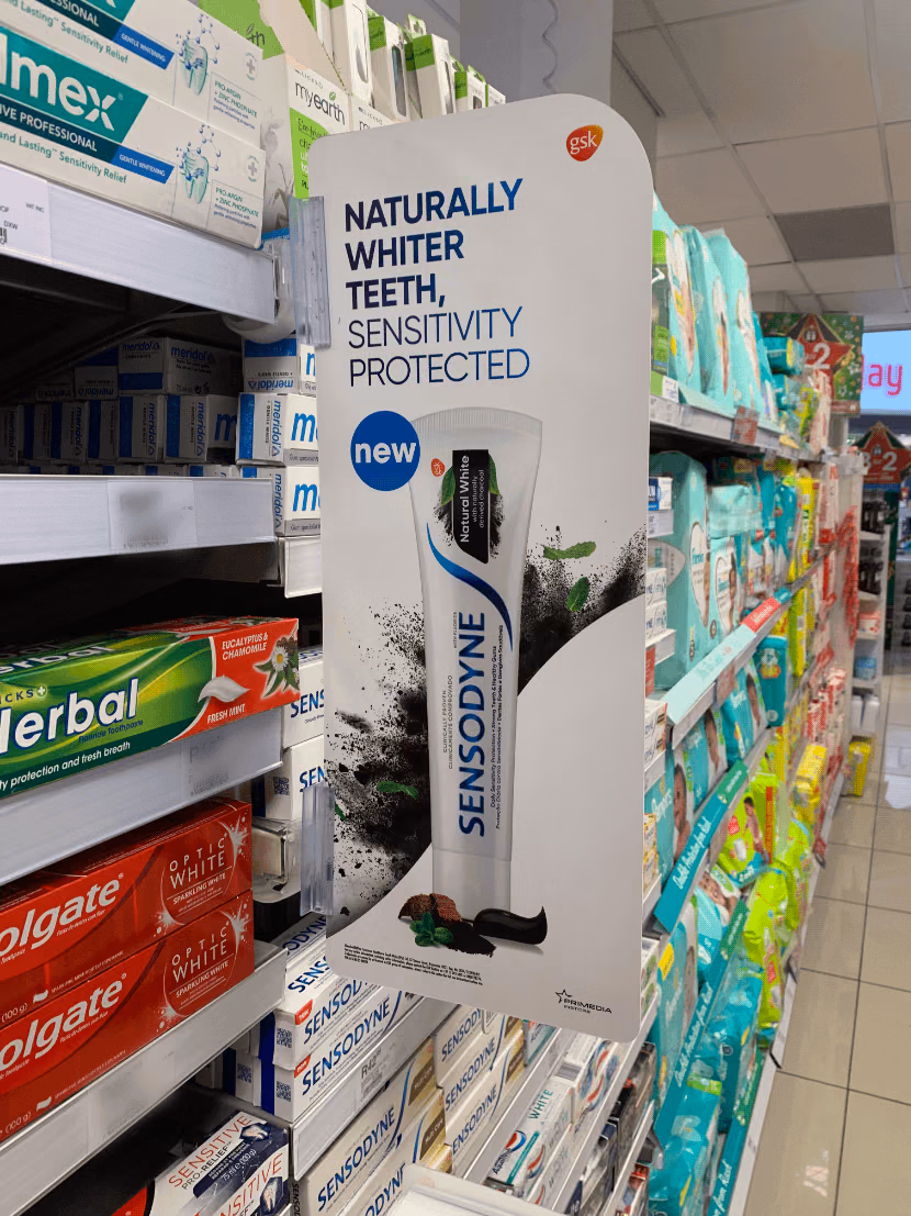 Store shelf with various toothpaste brands and a Sensodyne Natural White charcoal toothpaste advertisement.
