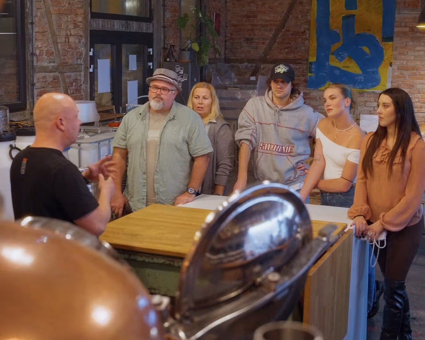 Skupina lidí poslouchá muže v černém tričku, který mluví v industriálním prostoru destilerie Garage22.