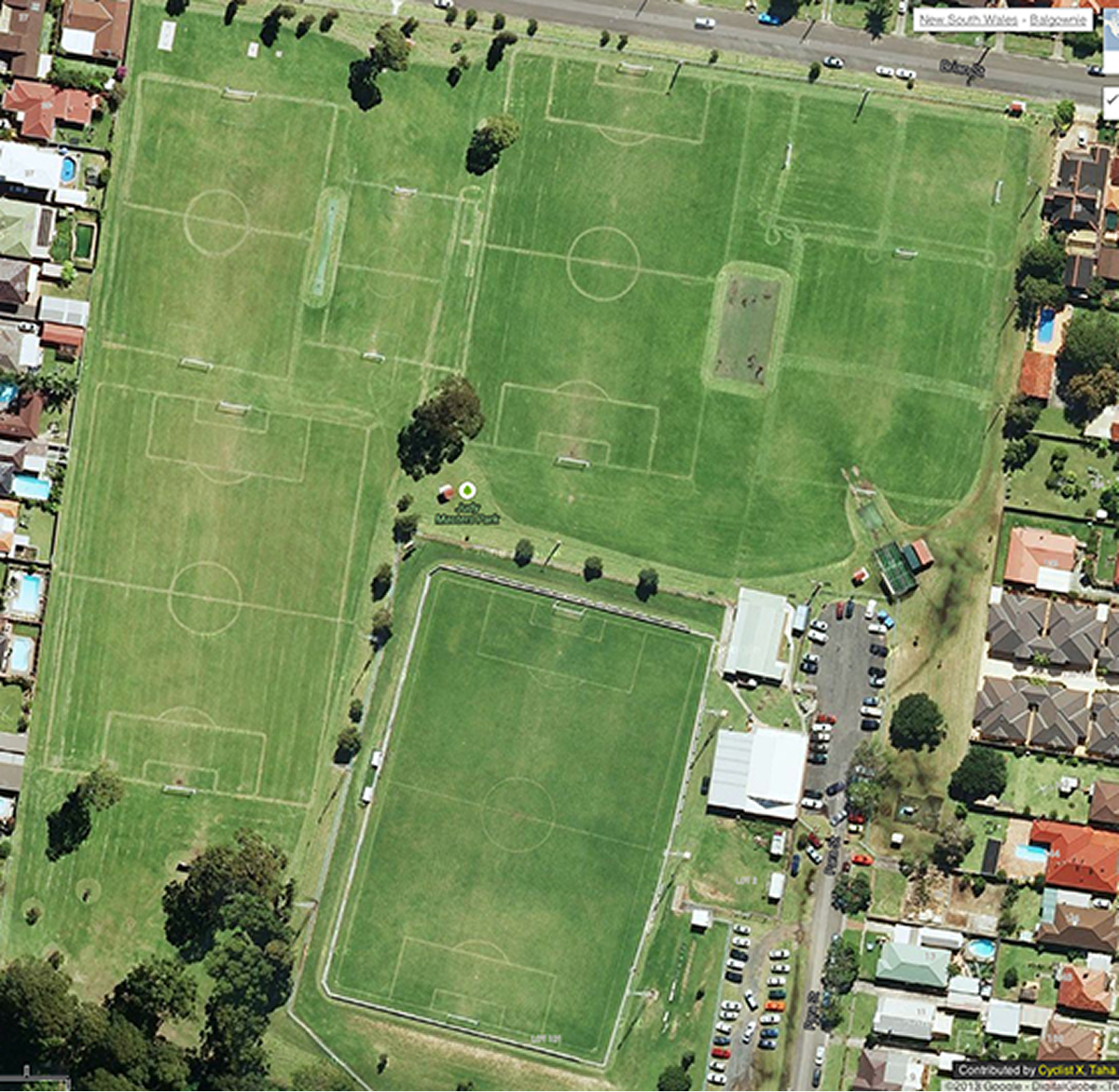 Aerial view of multiple soccer fields with goals and markings surrounded by residential houses and parking lots.