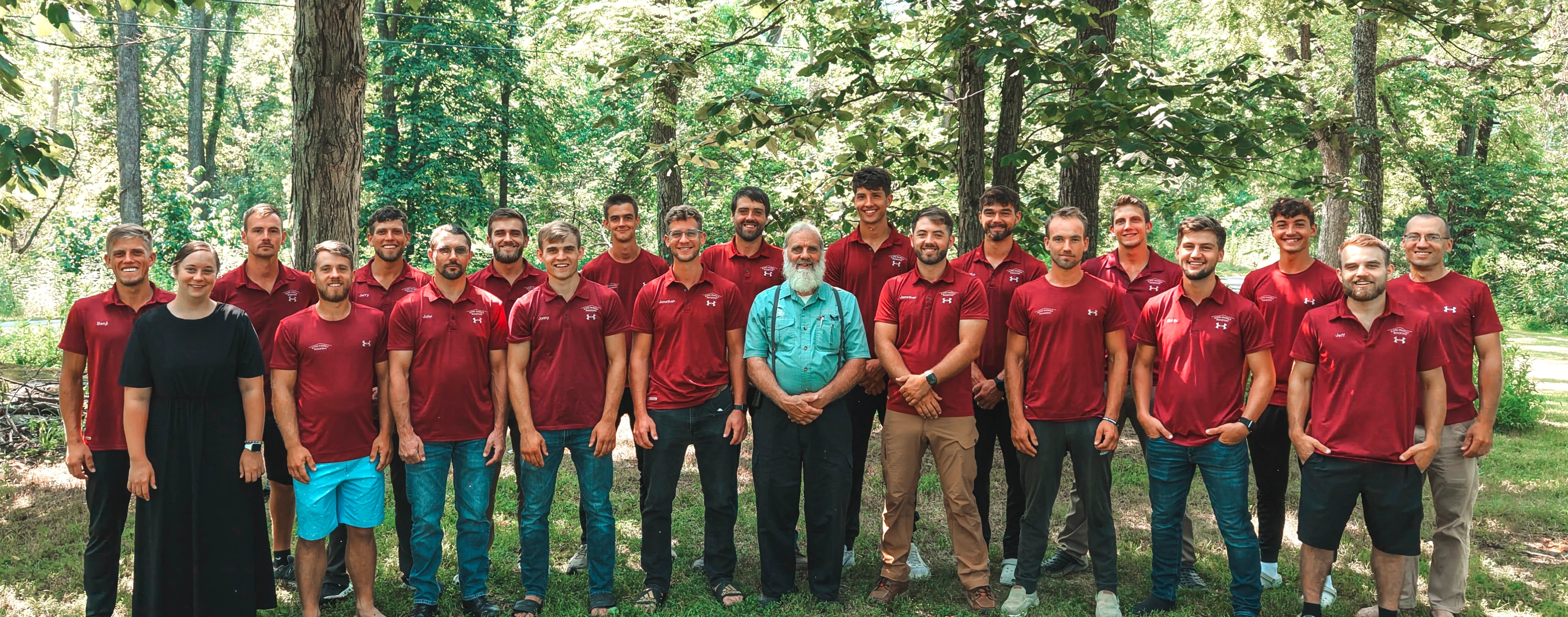 the King Family Roofing team stand in two rows outdoors, wearing matching red polo shirts, with trees and greenery in the background.