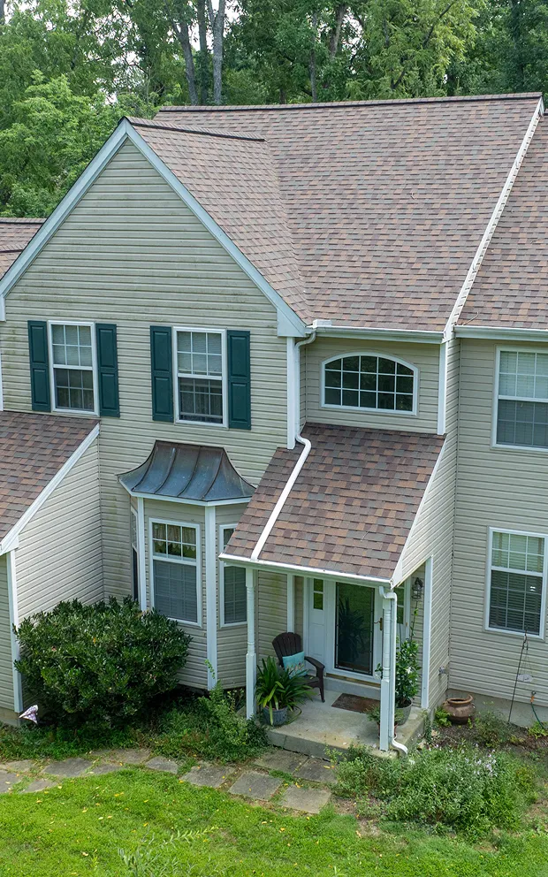 Two-story beige house with green shutters, brand new brown shingle roof, and covered front porch.