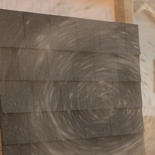 Close-up of gray asphalt roof shingles being tested with swirling wind.
