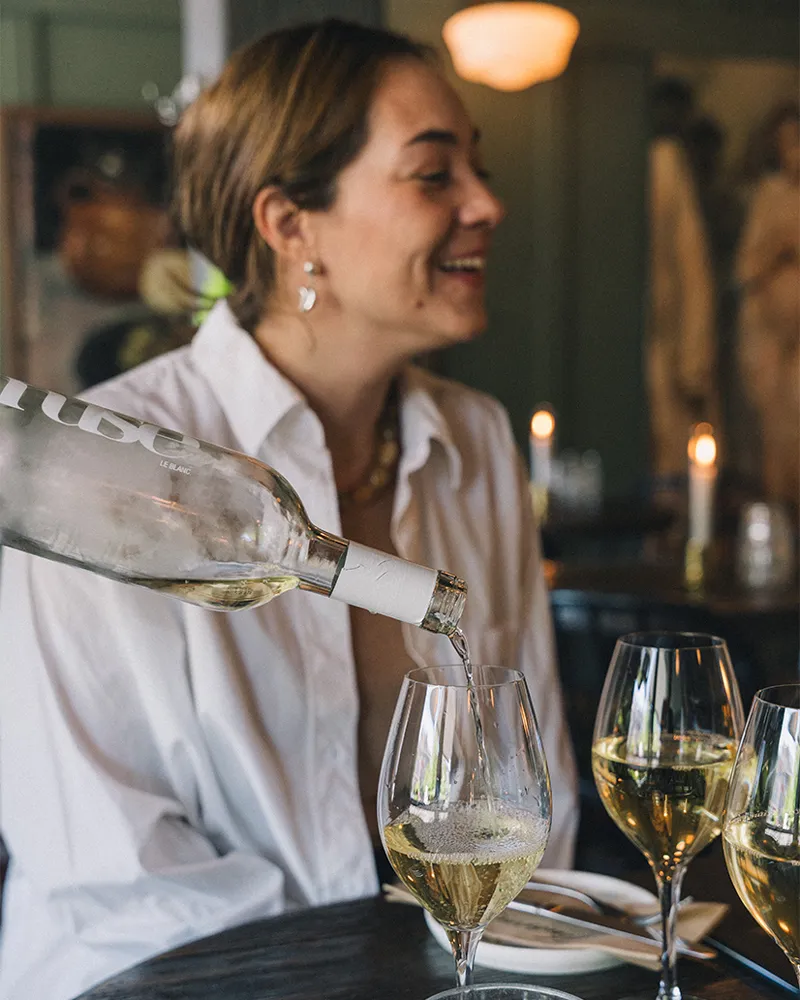 Kvinna som ler på en restaurang medan vitt vin hälls upp i ett glas på ett bord med tända ljus.