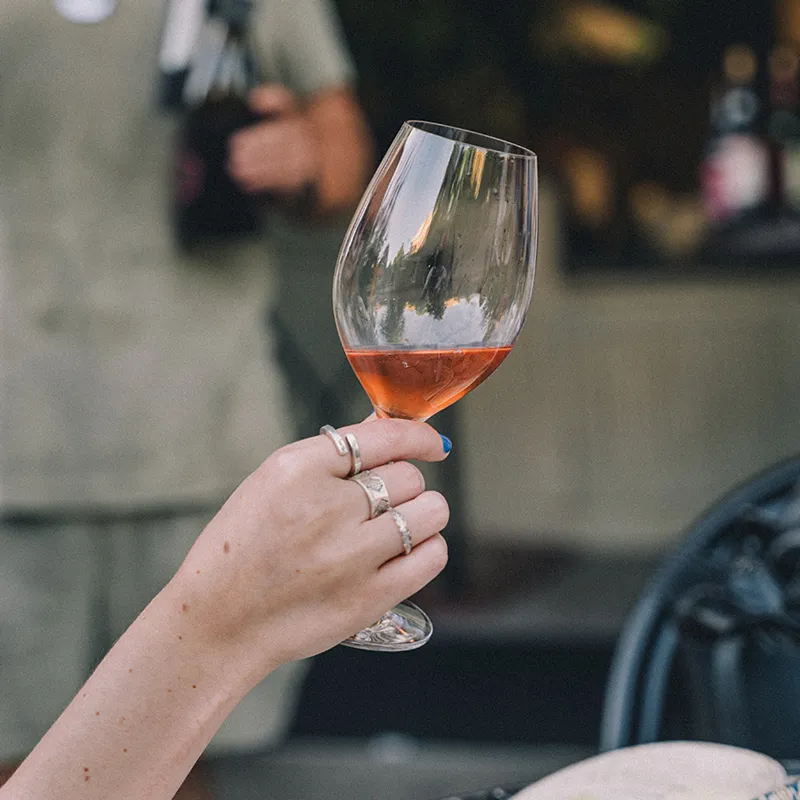 Hand med flera ringar som håller ett vinglas med rosévin.