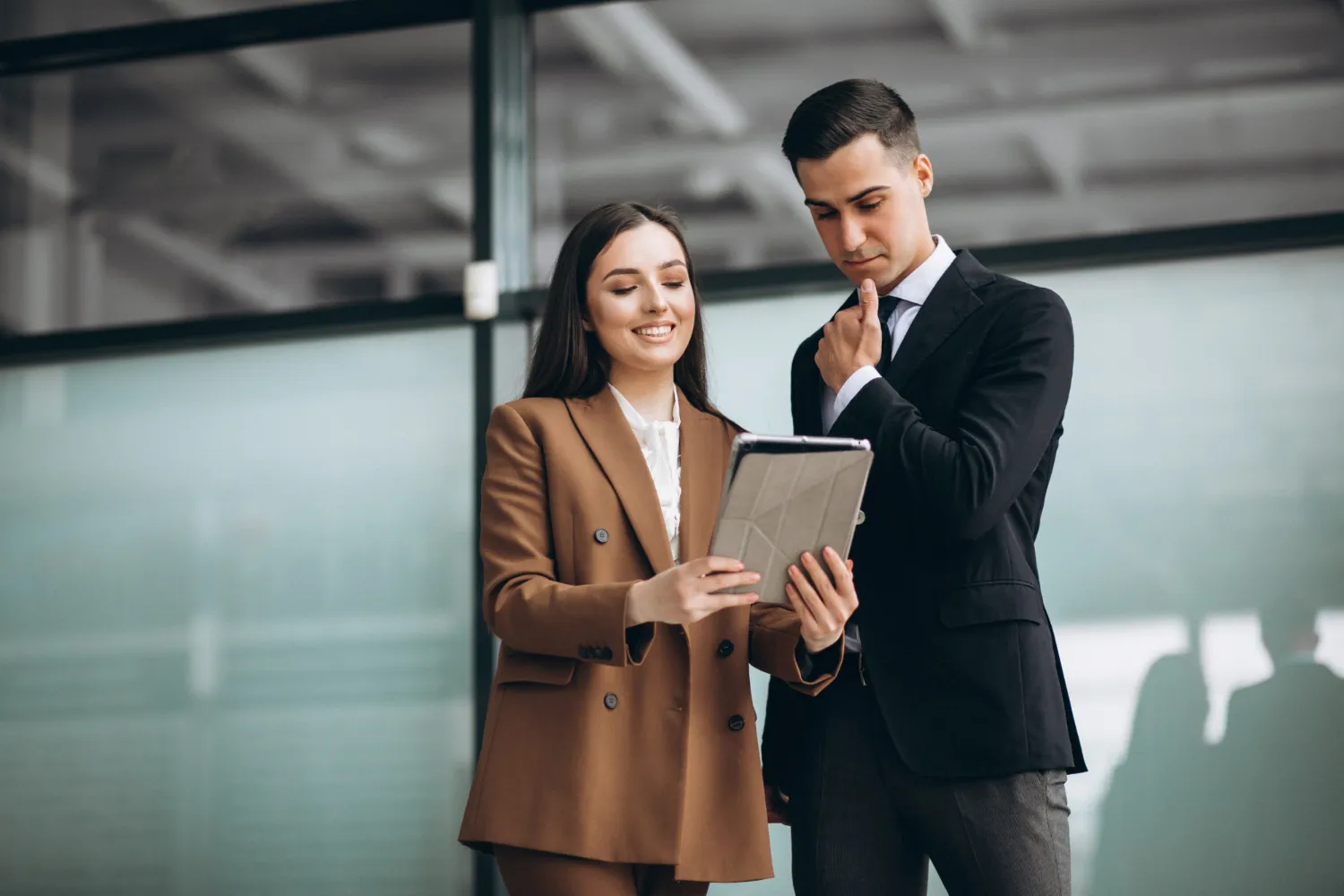 Two business professionals reviewing information on a tablet together in a modern office setting.