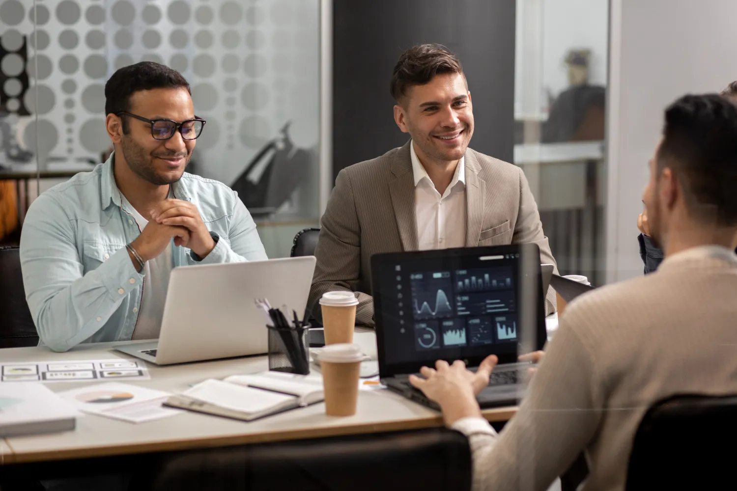 Three men having a business meeting around a table with laptops, coffee cups, and documents.