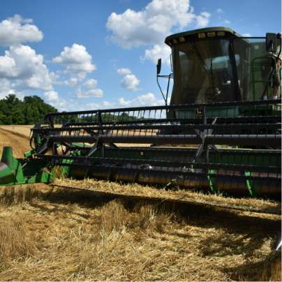 Un tracteur vert avec une grande lame à l'avant qui récolte le blé