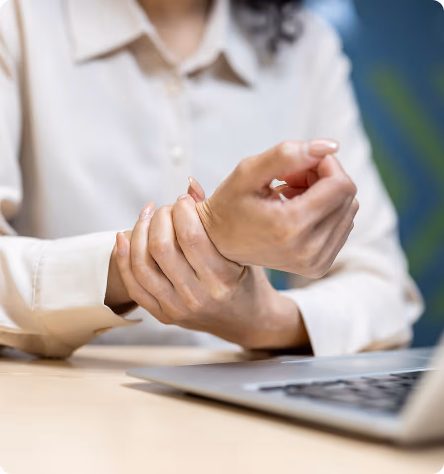 Person holding their wrist in pain while sitting at a desk with a laptop.