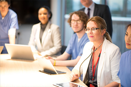medical professionals sitting around a table with laptops and tablets