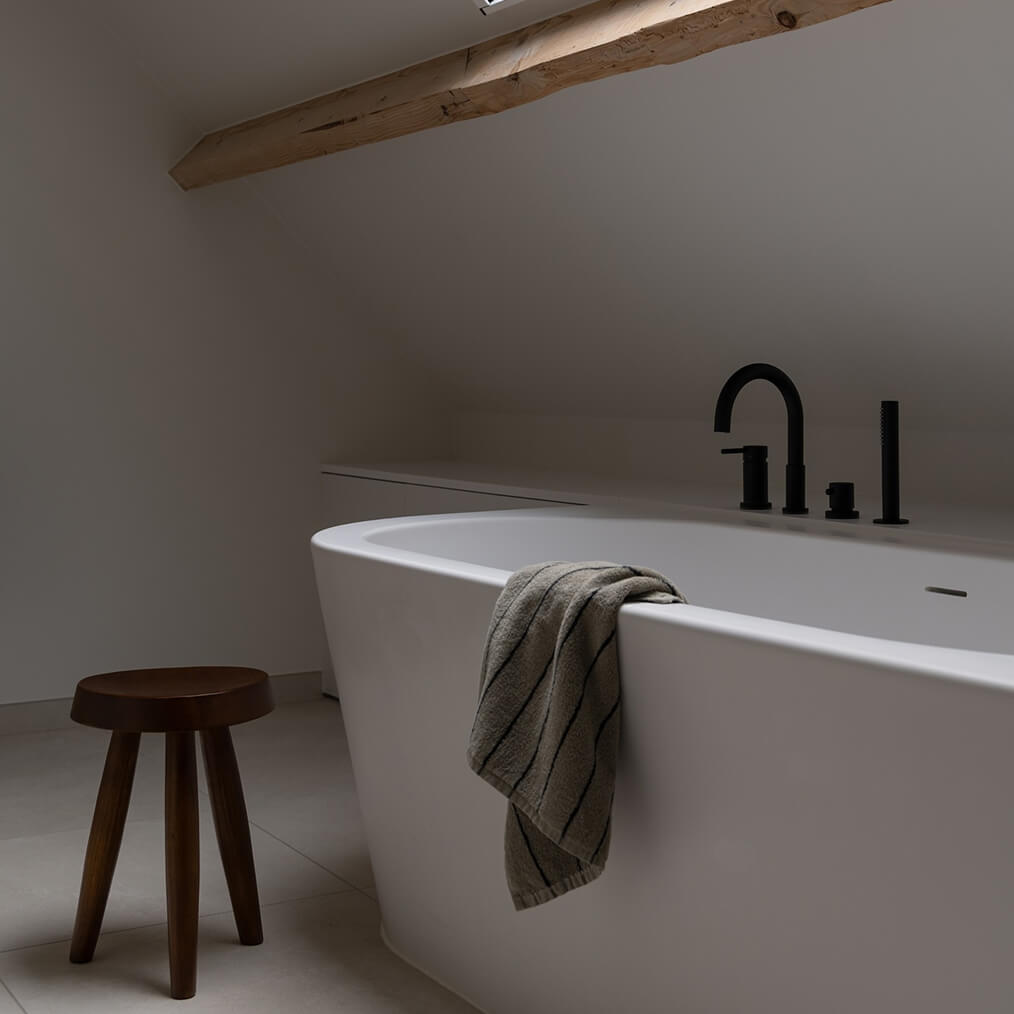 Detailfoto van een vernieuwde badkamer na een renovatie. Hier zie je het bad dat onder de houten gordingen van het dak zit.