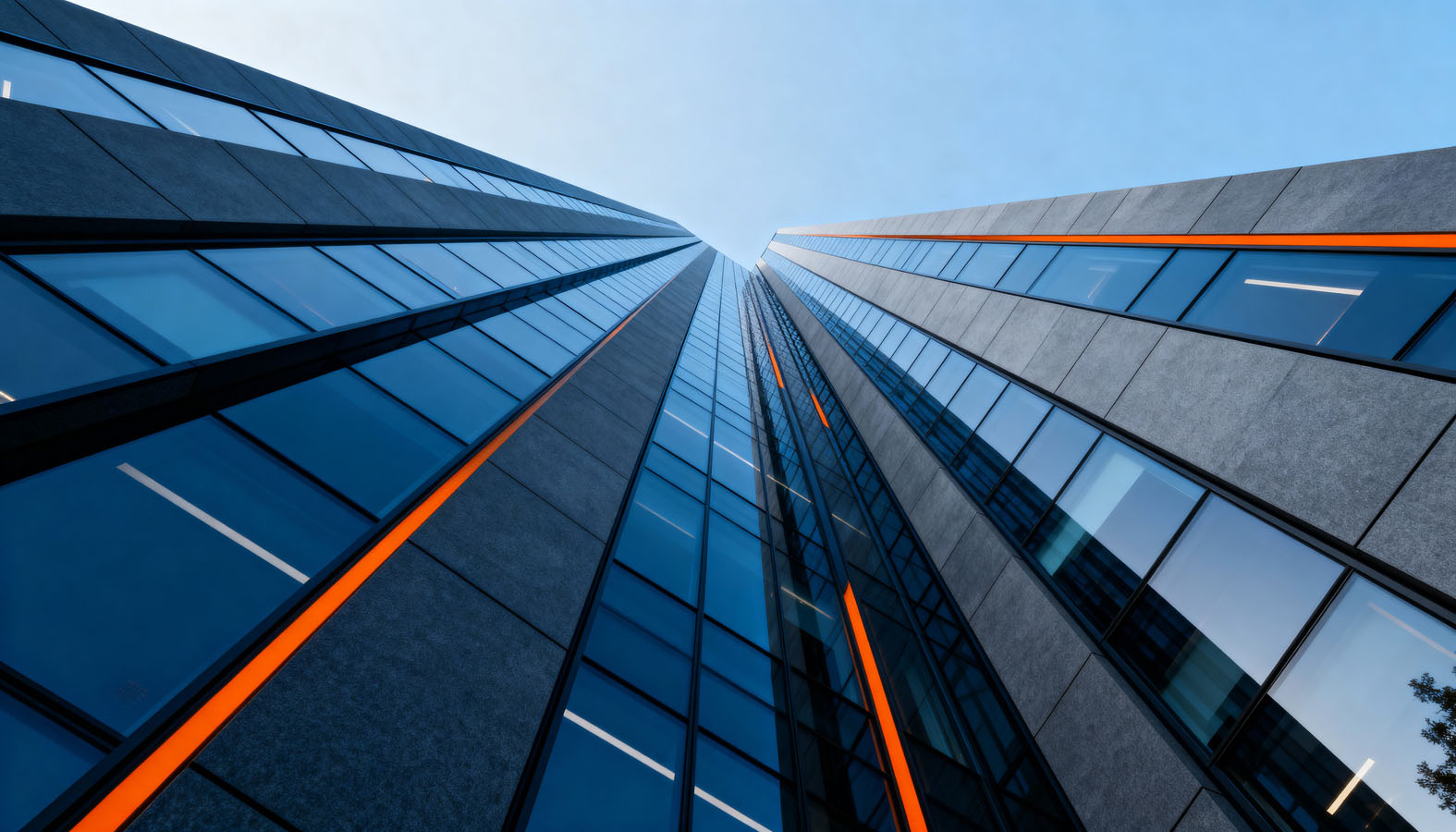 View looking up along modern glass and concrete skyscraper facades with vertical orange light strips.