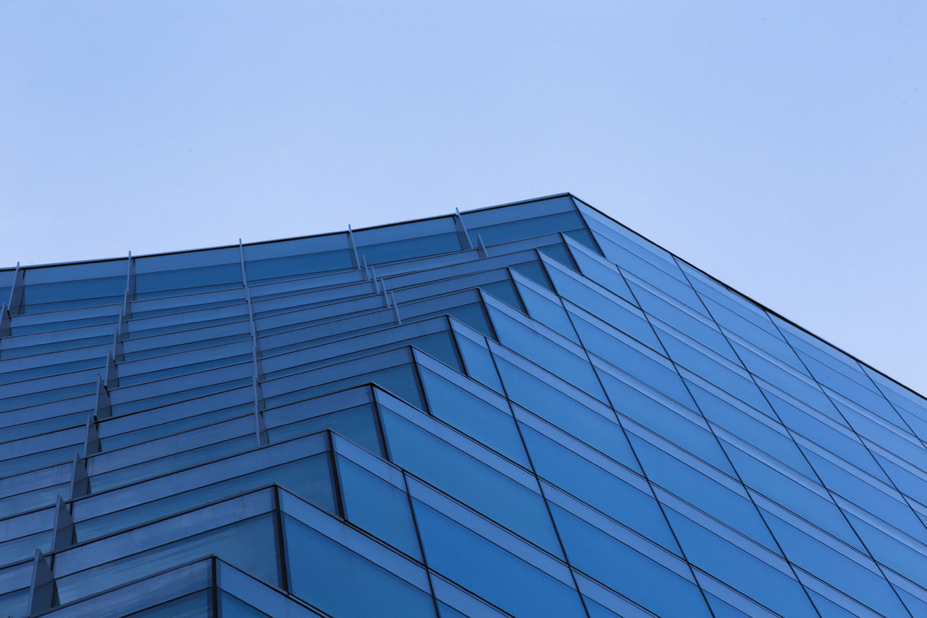 Upward view of a modern glass building with a stepped, angular facade against a clear blue sky.