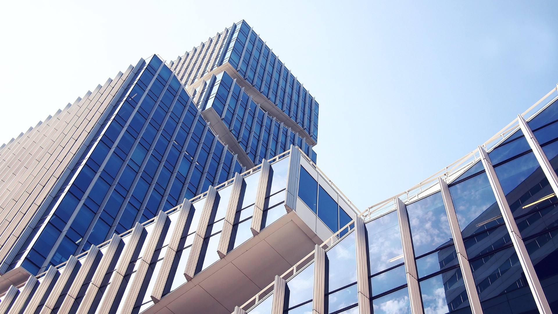 Modern glass office building with reflective windows against a clear blue sky.