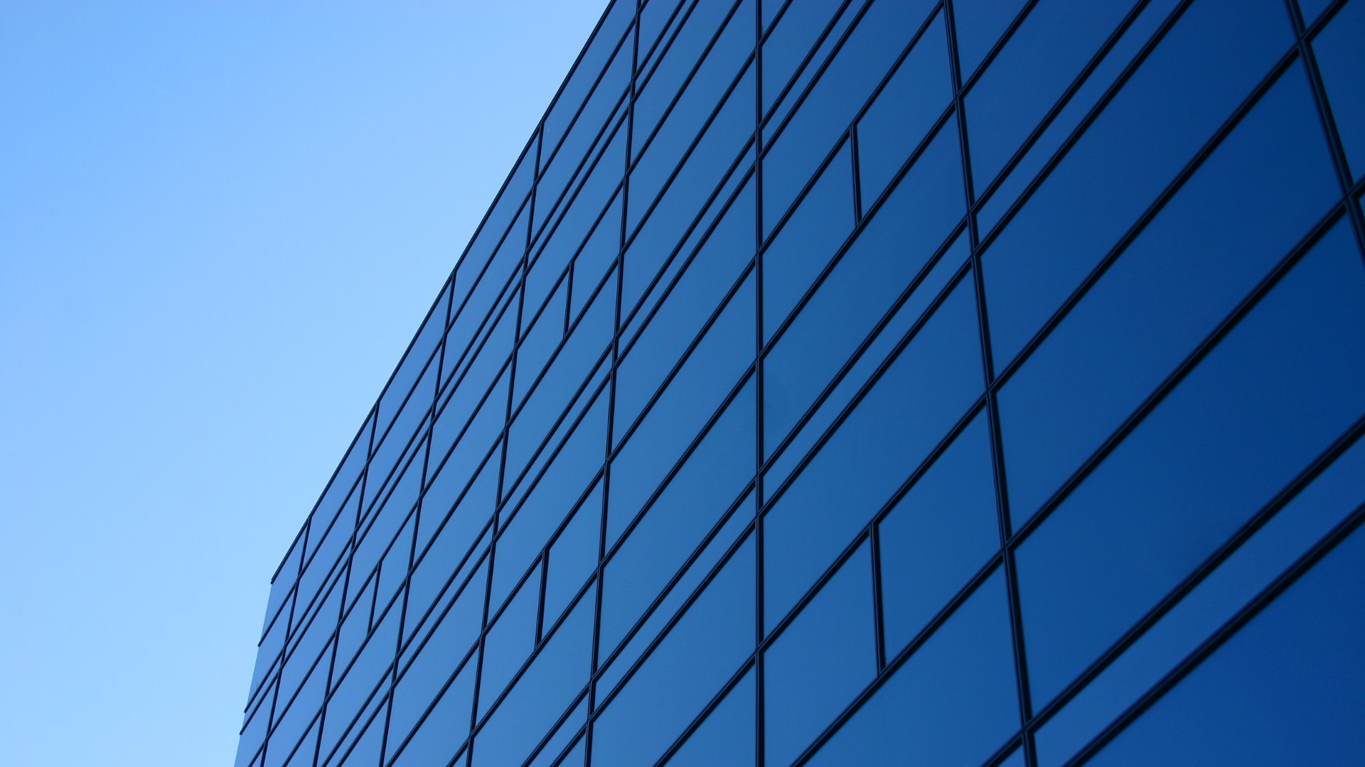 Modern office building facade with large reflective blue glass windows under clear sky.