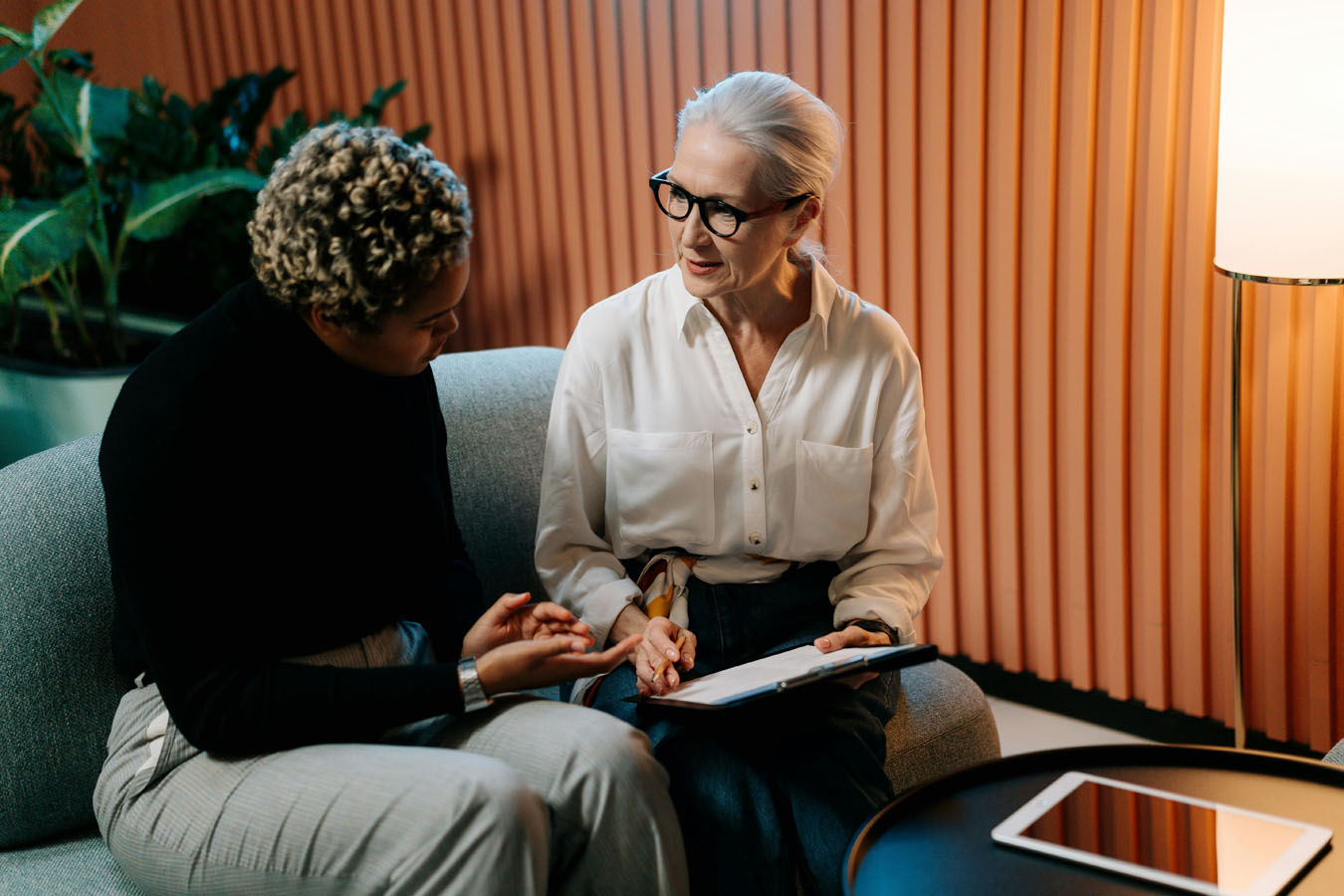 Two women sitting on a couch talking to each other.
