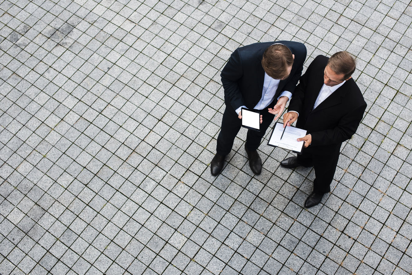 Two men in suits are looking at a piece of paper.