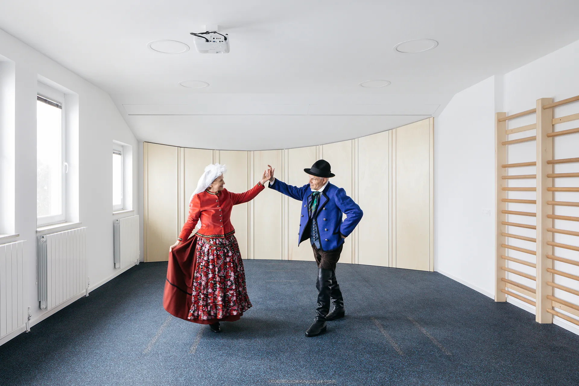 fotografija večnamenske dvorane, v kateri pleše par v folklornih oblačilih