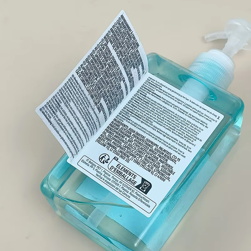 Transparent pump bottle filled with blue liquid soap and a folded label with ingredient and packaging information.