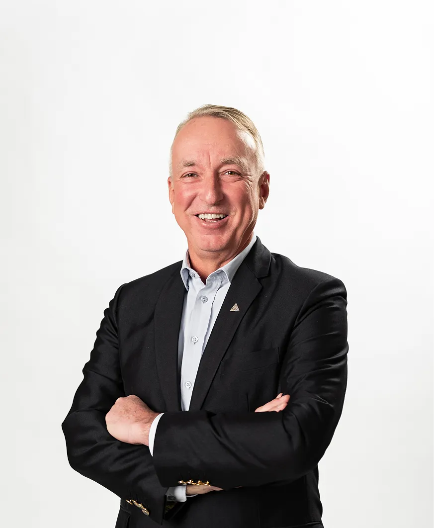 Smiling middle-aged man in black suit with arms crossed against a white background.