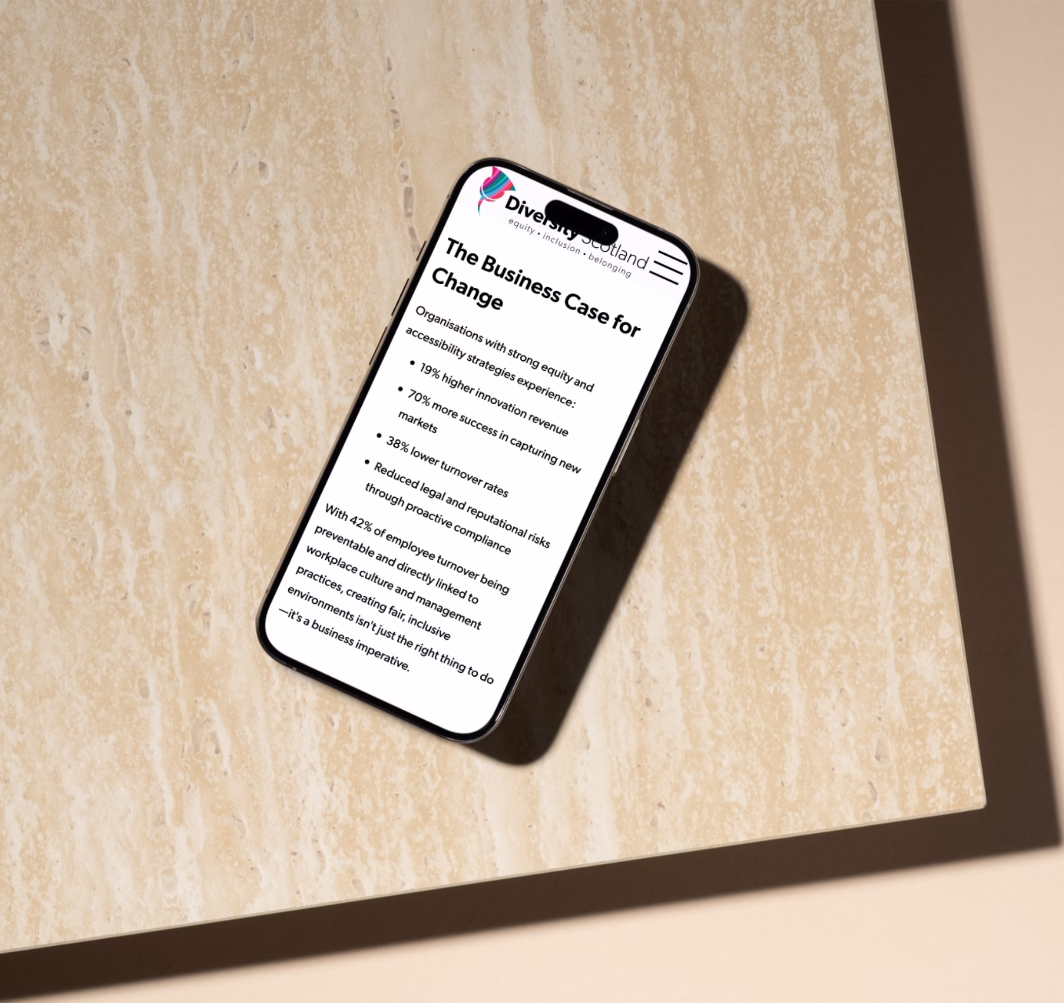 Mobile on a table showing the Diversity Scotland website, with dark text on a light background, logo on the top left and hamburger menu in the top right corner.