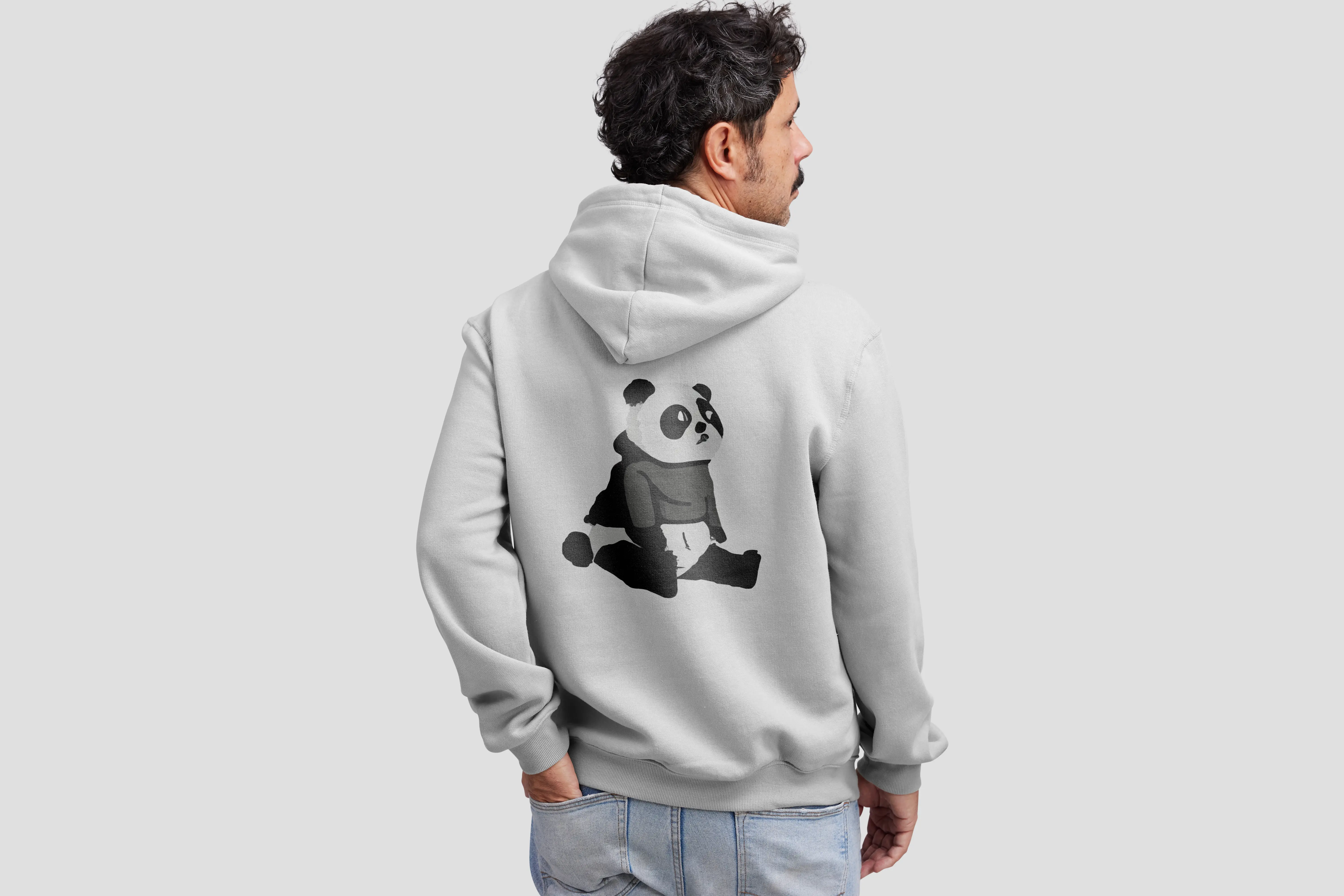 Man with curly hair seen from behind wearing a light gray hoodie featuring a black and white panda graphic sitting on the back.