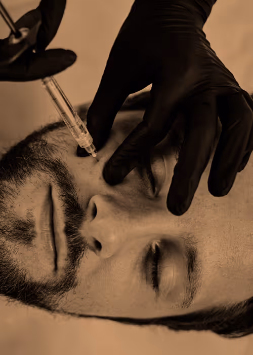 A person with a beard receives a facial injection from a professional wearing black gloves.