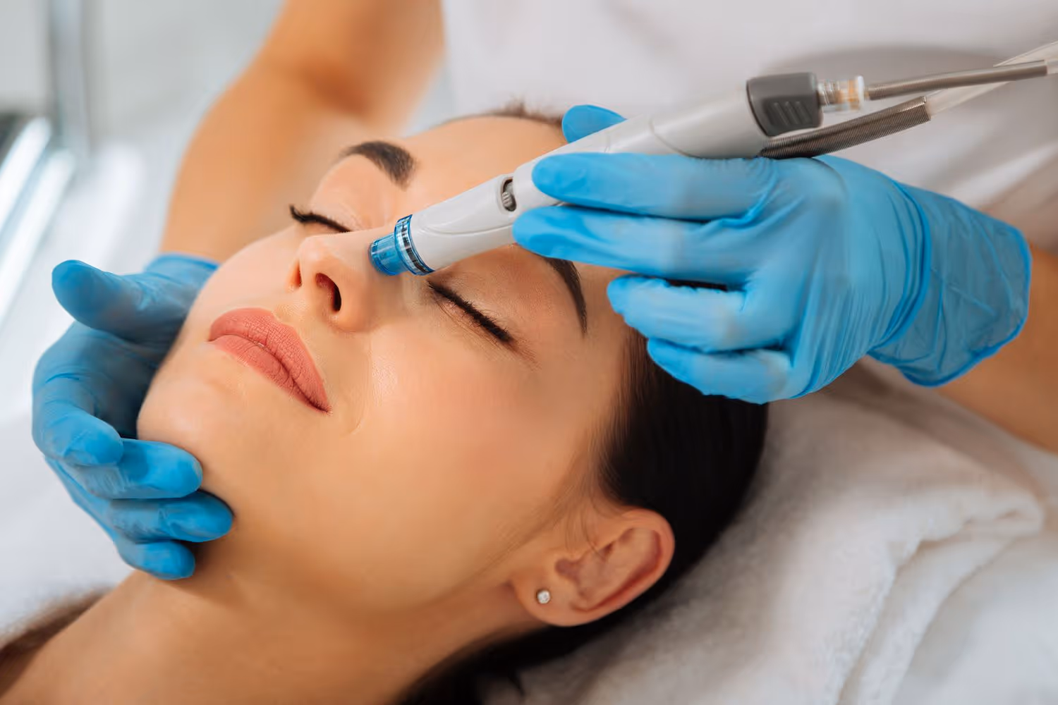 Person receiving a facial treatment, technician using a device on their face, wearing blue gloves.