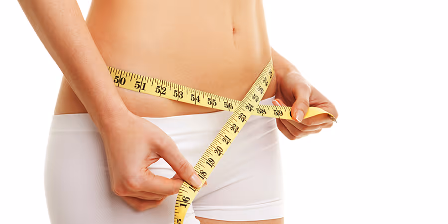 A person measures their waist with a yellow tape measure, wearing white shorts.