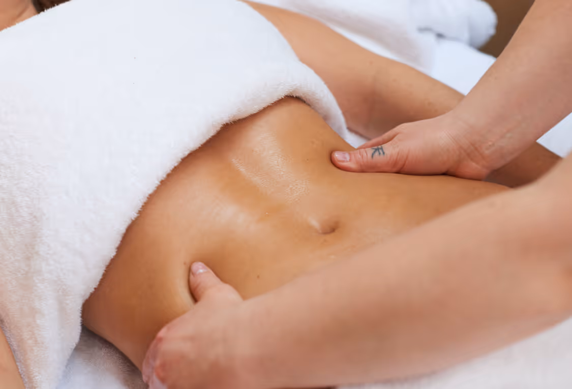 Person receiving an abdominal massage under a white towel.