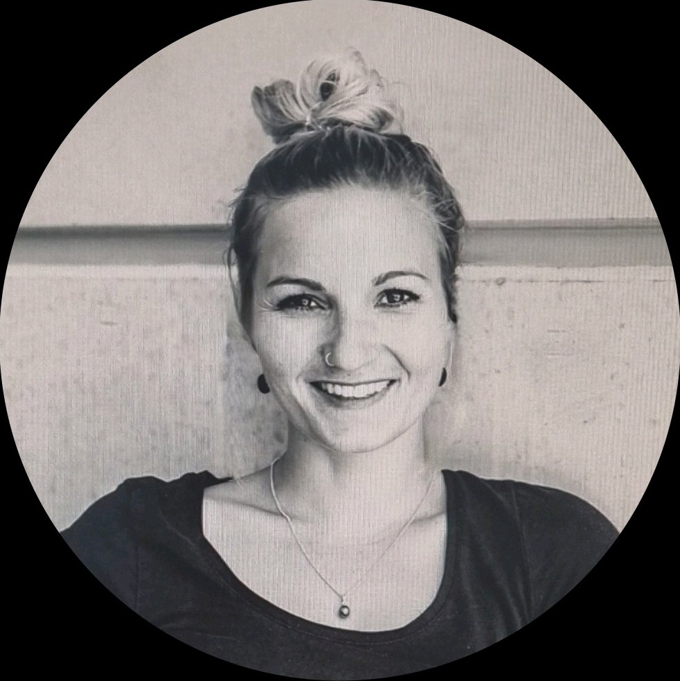 Black and white portrait of a smiling woman with a top bun hairstyle, wearing a dark shirt and a necklace.