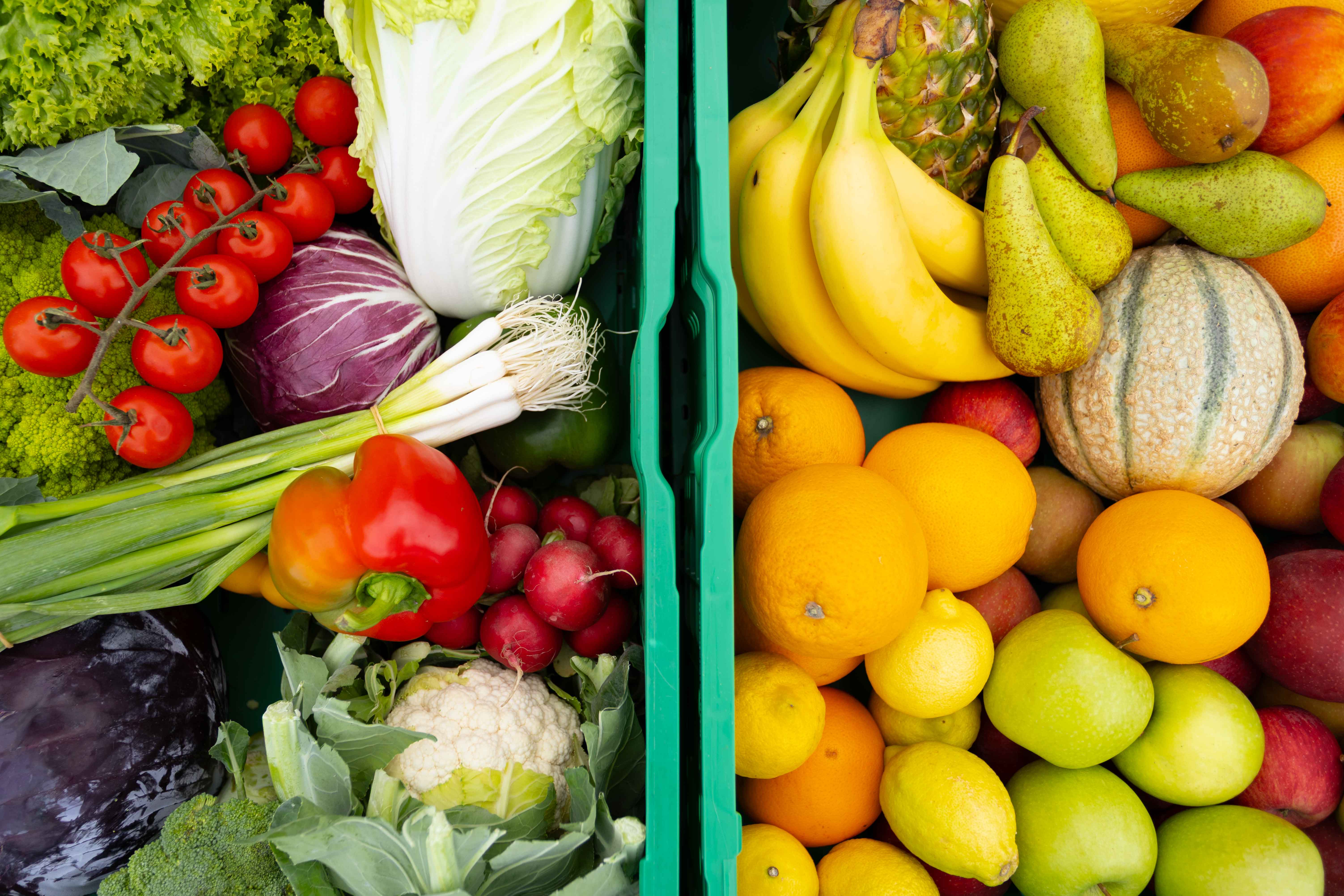 Zwei grüne Kisten mit frischem Gemüse links und Obst rechts, darunter Tomaten, Paprika, Radieschen, Bananen, Birnen, Orangen und Äpfel.