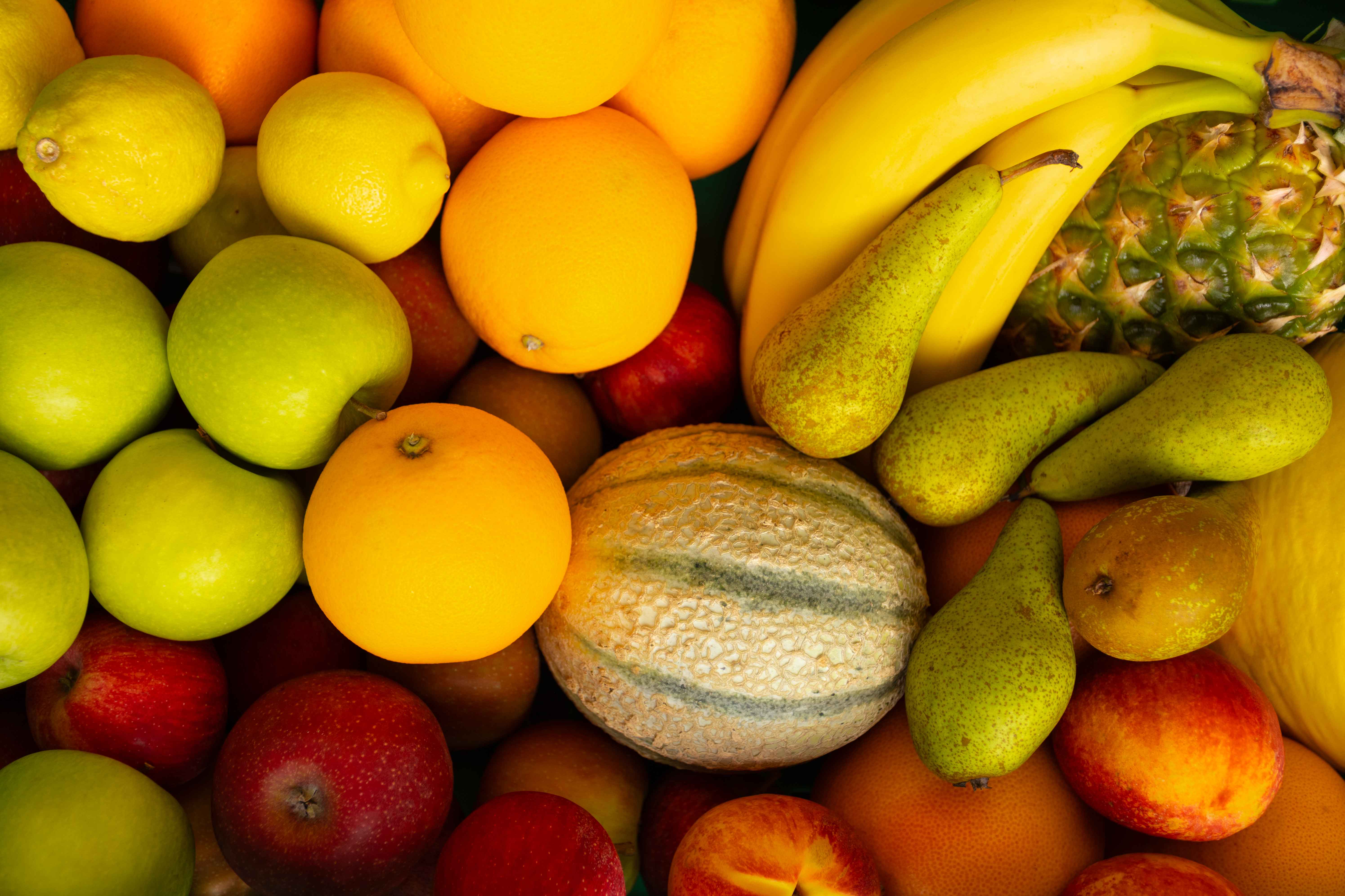 Verschiedene frische Früchte, darunter grüne und rote Äpfel, Orangen, Birnen, Bananen, eine Honigmelone und eine Ananas.