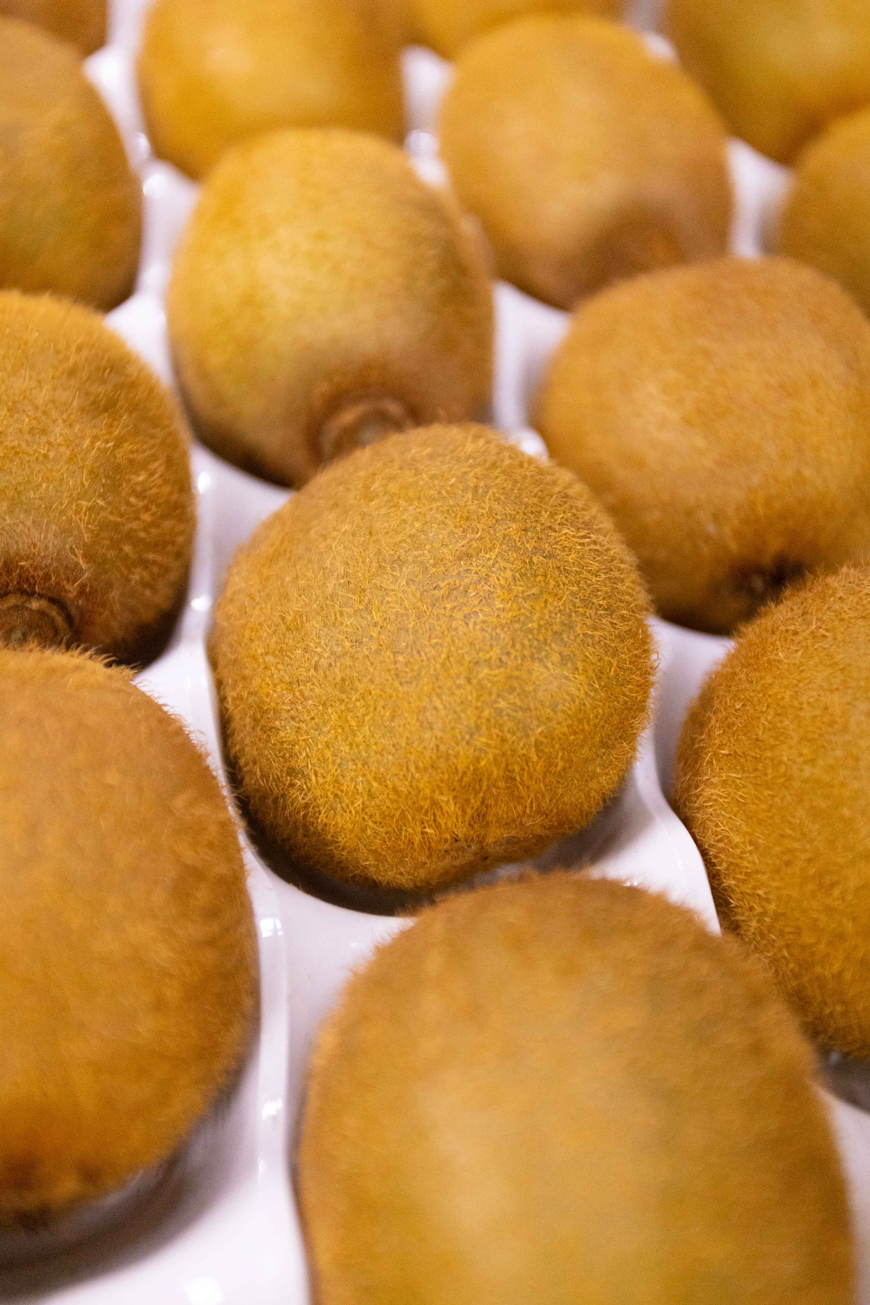 Nahaufnahme von mehreren braunen, pelzigen Kiwis in einer weißen Verpackung.