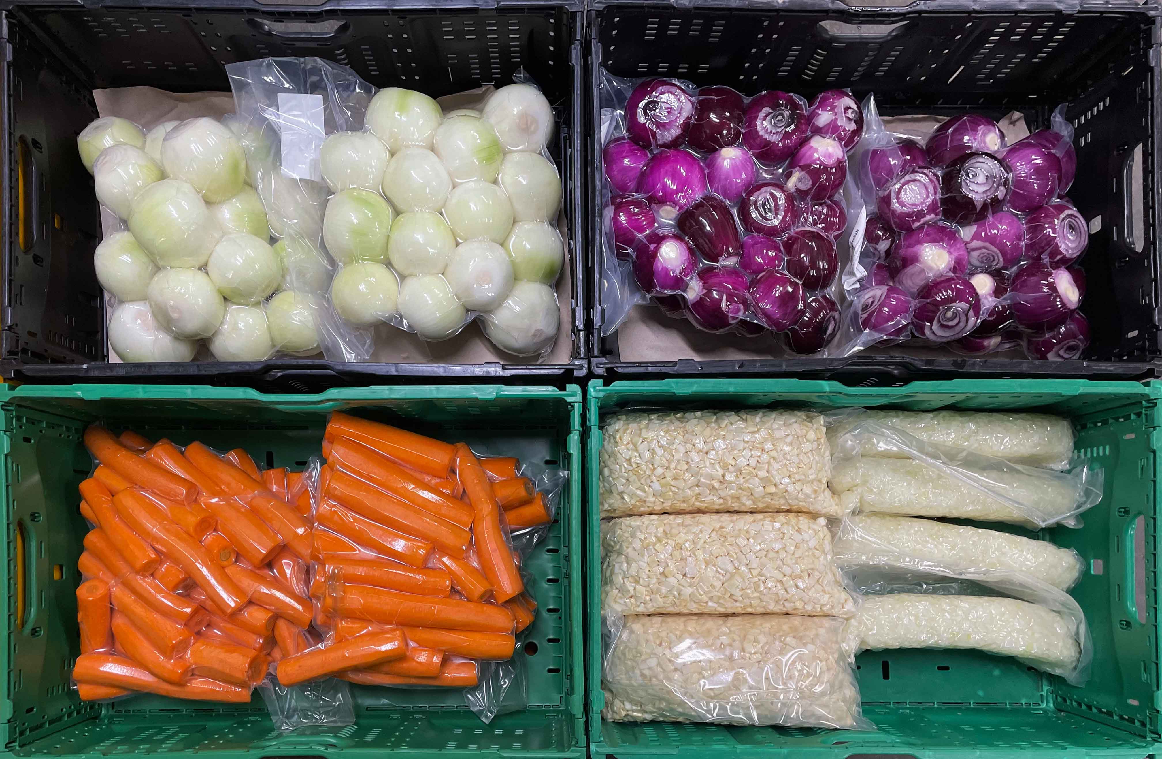 Verpackte weiße und rote Zwiebeln, geschnittene Karotten und vakuumverpackter gehackter Kohl in Kunststoffkisten.