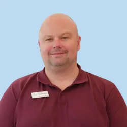 Lächelnder Mann in rotem Poloshirt mit Namensschild vor blauem Hintergrund