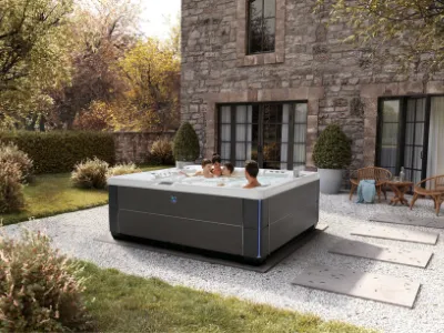Moderner Whirlpool auf Steinterrasse neben Natursteinhaus im Herbstgarten