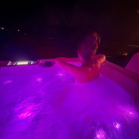 Person entspannt sich im violett beleuchteten Whirlpool bei Nacht