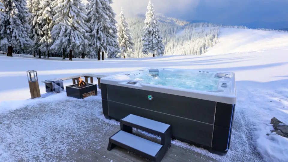 Whirlpool im verschneiten Winterwald mit Lagerfeuer und Bergen im Hintergrund