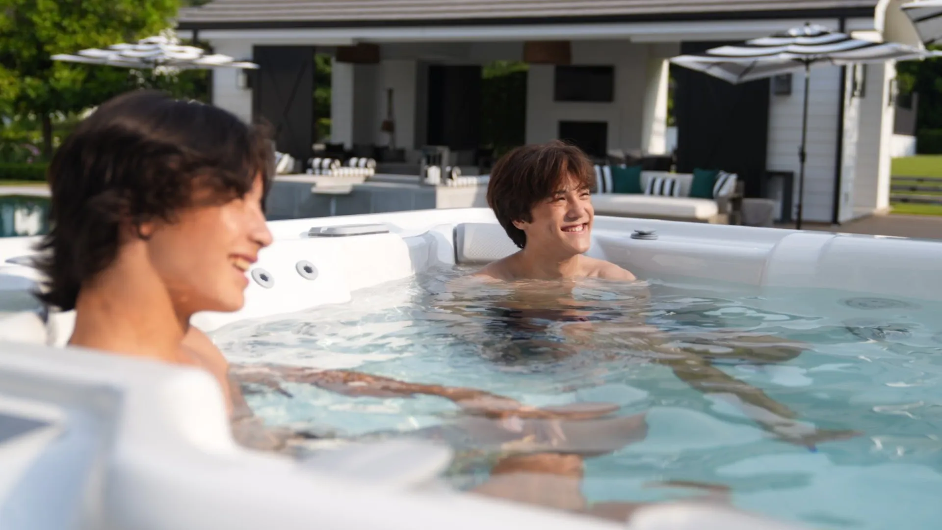 Zwei Personen entspannen in einem Whirlpool mit Poolhaus im Hintergrund
