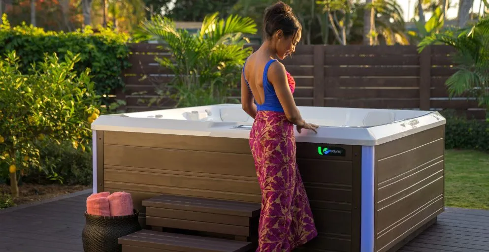 Person steht neben einem Whirlpool im Garten mit tropischen Pflanzen im Hintergrund
