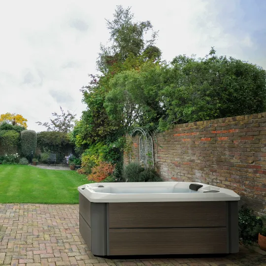 Whirlpool auf Backsteinpflaster im grünen Garten mit Ziegelmauer