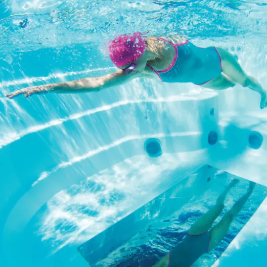 Schwimmerin mit rosa Badekappe gleitet unter Wasser im blauen Pool