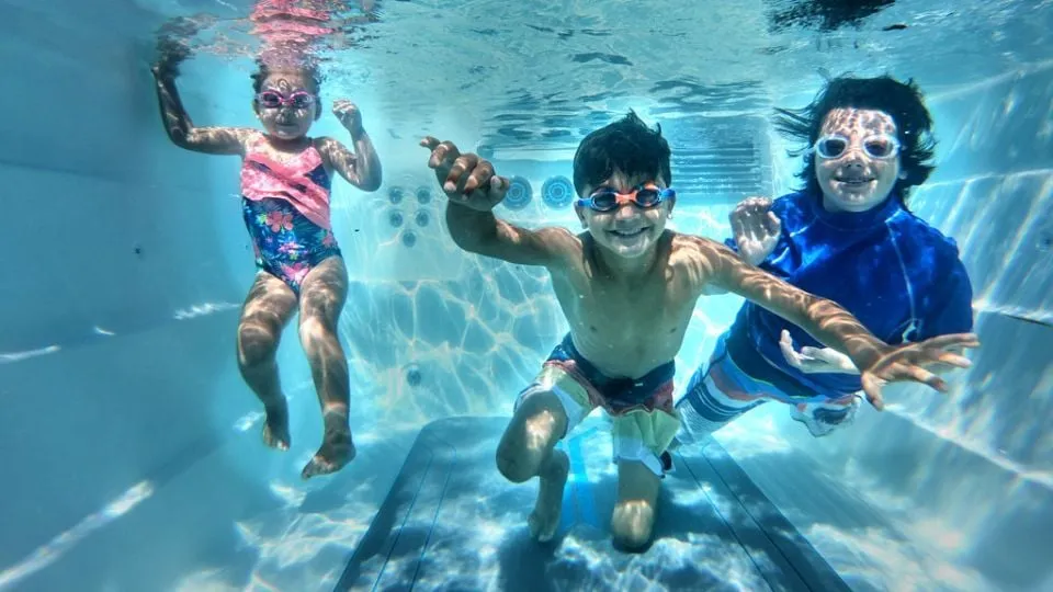 Drei Kinder schwimmen unter Wasser mit Taucherbrille und spielerischer Freude