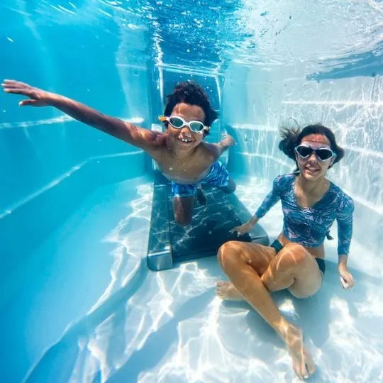 Zwei Personen schwimmen unter Wasser mit Schwimmbrillen in blauem Pool